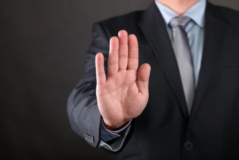 Muž v obleku s nataženou rukou a dlaní znázorňující stop.
