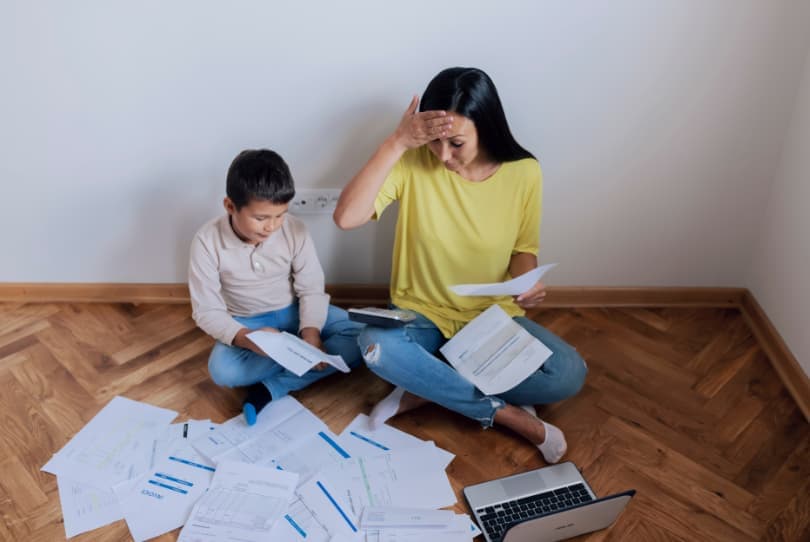 Žena s dítětem sedící na podlaze s dokumenty a notebookem.